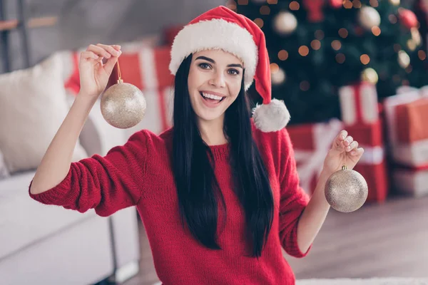 Photo of funny lovely lady hold two golden baubles open mouth wear santa headwear red sweater in decorated living room indoors — Stock Photo, Image