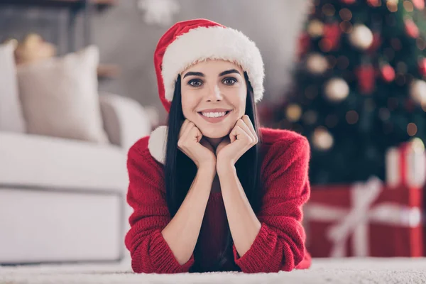 Foto da menina encantadora punhos de tapete leigos queixo de dente sorrindo desgaste santa headwear pulôver vermelho na sala de estar decorada dentro de casa — Fotografia de Stock