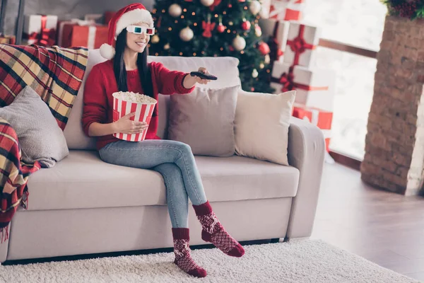 Photo of lady sit couch hold remote control popcorn box wear 3d specs santa cap red sweater jeans socks in decorated living room indoors — Stock Photo, Image