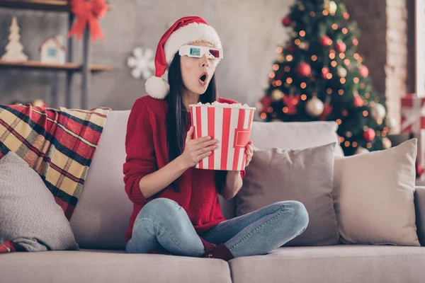 Photo of lady sit sofa open mouth hold pop corn bucket wear 3d specs santa cap red pullover jeans in decorated living room indoors — Stock Photo, Image