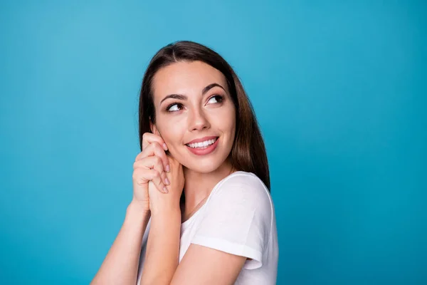 Närbild profil foto av charmiga söta vackra dam hålla armarna nära kinderna ansikte strålande leende överlycklig utseende sida upp tomt utrymme slitage casual vit t-shirt isolerad blå färg bakgrund — Stockfoto