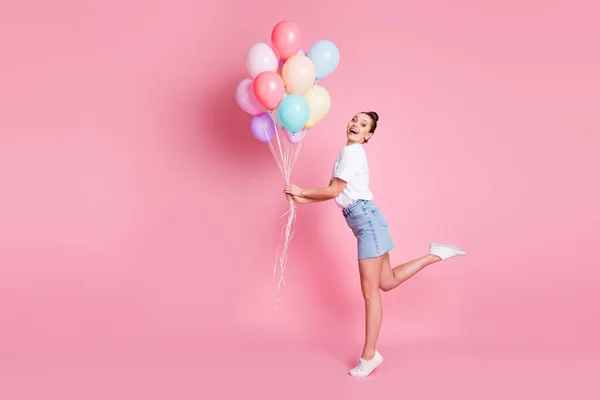 Full size profil fotografie atraktivní dáma hezká houska letní dovolená dobrá nálada držet mnoho vzduchové balónky oslavy nosit bílé tričko mini sukně boty izolované růžové barvy pozadí — Stock fotografie