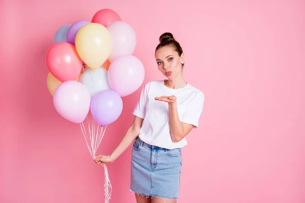 Photo of attractive pretty lady pretty bun good mood hold many air balloons birthday celebration sending air kisses wear white t-shirt denim mini skirt isolated pink color background