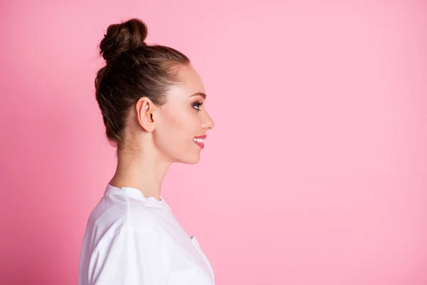 Närbild profil foto av attraktiv dam rolig bulle frisyr ser sida tomt utrymme glad uttryck gott humör strålande leende bära vit t-shirt isolerad pastell rosa färg bakgrund — Stockfoto