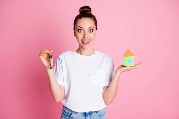 Foto van aantrekkelijke dame broodje kapsel vasthouden hand klein papieren huis sleutelhanger onroerend goed bewegende droom huis lage prijs open mond slijtage wit t-shirt geïsoleerde pastel roze kleur achtergrond — Stockfoto