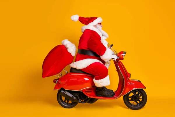 Volledige lengte profiel zijkant foto van de kerstman met baard rijden motor snel leveren x-mas kerst zak presenteert dragen rood zonneglas kap geïsoleerde heldere glans kleur achtergrond — Stockfoto