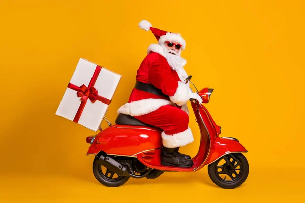 Full length profile side photo of grey white hair bearded santa claus ride drive bike deliver gift box x-mas christmas night wear red headwear isolated yellow color background — Stock Photo, Image