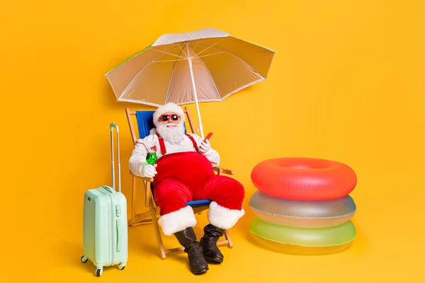 원문 기사보기 하얀 머리 수염 산타 클라우스가 크리스마스 선물을 준비하고 있는 칵테일셀 스마트 폰빨간 코스튬 모자를 쓰고 있다. — 스톡 사진