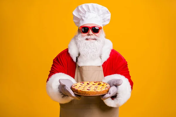 Zdjęcie Santa Claus szef kuchni nakrycia głowy dziadek szara broda trzymać gotowy świeży słodki duży placek z dżemem nosić x-mas kostium rękawice okulary okulary fartuch izolowany żółty kolor tło — Zdjęcie stockowe