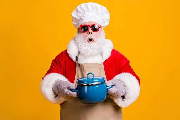 Foto von schockiert Dummheit Opa Kochmütze halten heiße Pfanne Handschuhe Koch Vorbereitung Familienrezept vermissen späten Abfall Zeit tragen x-mas roten Kostümmantel Sonne Spezifikationen Schürze isoliert gelbe Farbe Hintergrund — Stockfoto