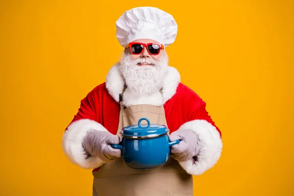 Photo of wesoły przyjazny Santa dziadek szef kuchni nakrycia głowy trzymać gorące rękawice pan gotować przygotowanie tradycji rodzinnej przepis nosić czerwony kostium płaszcz okulary fartuch izolowany żółty kolor tło — Zdjęcie stockowe