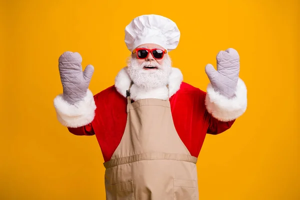 Zdjecie podekscytowany wesoły Santa dziadek szary broda szef kuchni nakrycia głowy piec gotowanie podnieść ręce garnki rękawice nosić czerwony kostium płaszcz rękawice okulary okulary okulary fartuch izolowany żółty kolor tło — Zdjęcie stockowe