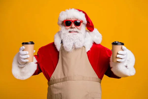 Close-up portret jego miły atrakcyjny wesoły wesoły kelner Santa gospodarstwa w rękach dwa kubki zamówić latte napój kakao dając porządek odizolowany jasny żywy blask żółty kolor tło — Zdjęcie stockowe