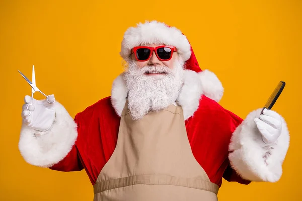 Close-up retrato de sua agradável atraente alegre alegre de cabelos grisalhos Papai Noel vestindo avental segurando em mãos ferramentas de coiffure equipamento isolado brilhante brilhante brilho vibrante cor amarela fundo — Fotografia de Stock