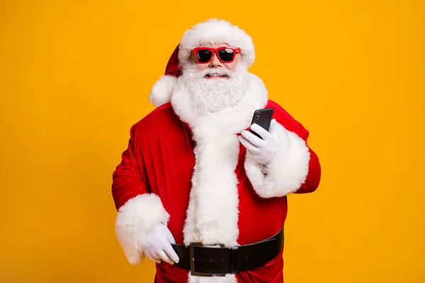 Portrait de son il agréable joyeux joyeux Père Noël en utilisant l'appareil gadget bavarder commande shopping service en ligne isolé sur lumineux éclat vif fond de couleur jaune vif — Photo