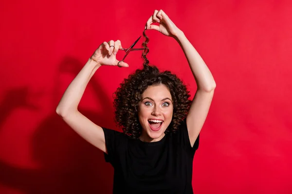 Retrato de menina atraente ondulado corte cabelo segurar tesoura desgaste preto t-shirt isolado no fundo de cor vermelha — Fotografia de Stock