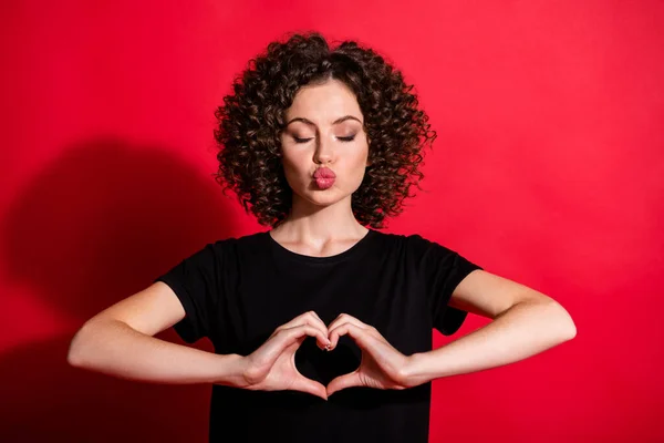 Foto de penteado ondulado pessoa olho fechado beijo você mostrar forma de coração casual preto t-shirt isolado no fundo de cor vermelha — Fotografia de Stock