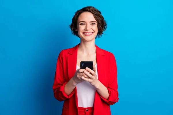 Retrato de atractiva dama de negocios de pelo castaño alegre usando gadget como seguir aislado sobre fondo de color azul brillante — Foto de Stock