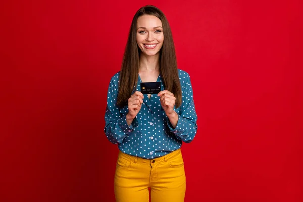 Retrato de chica alegre alegre atractiva sosteniendo en las manos tarjeta bancaria aislado sobre fondo de color rojo brillante —  Fotos de Stock