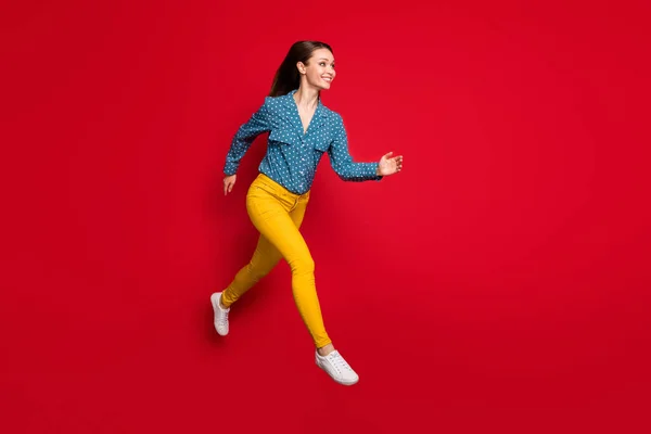 Полноразмерный вид на привлекательно сидящую жизнерадостную девушку, быстро бегущую по ярко-красному цветному фону — стоковое фото