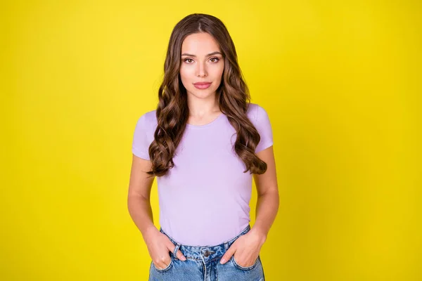 Retrato de conteúdo atraente menina de cabelos ondulados de mãos dadas em bolsos isolados no fundo de cor amarelo brilhante — Fotografia de Stock