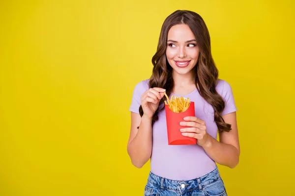 Portré vonzó vidám hullámos hajú lány élvezi eszik sült krumpli másolás tér elszigetelt élénk sárga színű háttér — Stock Fotó