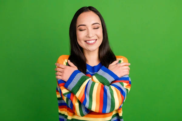 Retrato de cerca de la encantadora chica alegre soñadora que lleva un jersey cálido a rayas abrazándose aislada sobre un fondo de color verde vibrante —  Fotos de Stock