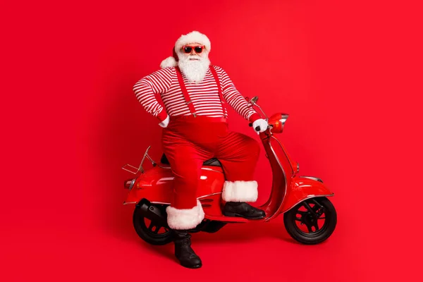 Фотографія дідуся сірої бороди біля ретро скутера холодний одяг Санта-Клауса підвіски для костюмів для костюмів Сонцезахисні смугасті чоботи для сорочок ізольований червоний кольоровий фон — стокове фото