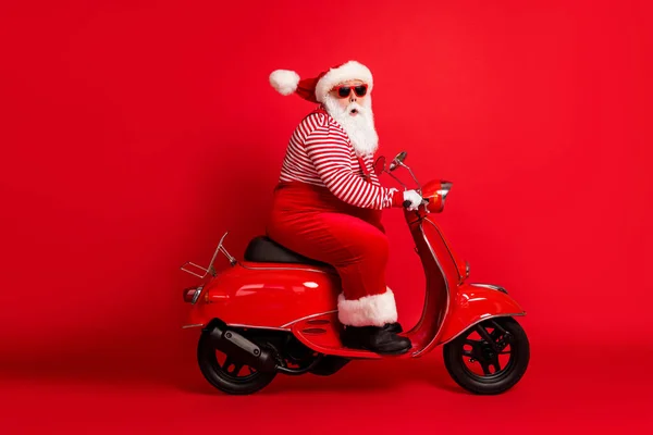 Heyecanlı gri sakallı eski motosiklet fotoğrafının tam boy profil fotoğrafı. Kameraya bak. Noel Baba 'nın Noel Baba' sı, Noel Baba 'nın kostüm askısı güneş gözlüğü çizgili gömlek kapağı, izole edilmiş kırmızı arka plan. — Stok fotoğraf