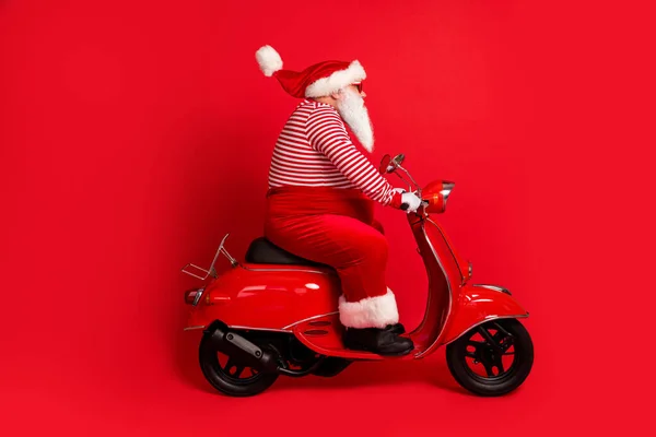 Foto profil lengkap dari kakek berjenggot abu-abu mengendarai sepeda motor vintage memakai kostum santa claus x-mas suspender kacamata garis-garis topi sarung tangan warna merah terisolasi latar belakang — Stok Foto