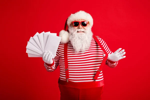 Фото деда седой бороды улыбка весело держать в руках конверты носить Санта-Клаус X-мас костюмы подтяжки солнцезащитные очки полосатая рубашка шапочка перчатки изолированные красный цвет фона — стоковое фото
