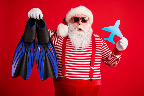 Photo of grandfather grey beard hold paper plane diving flippers shock wear santa claus x-mas costume suspenders sunglass striped shirt cap isolated red color background — Stock Photo, Image