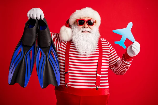 Photo of grandfather grey beard hold paper plane diving gear flippers wear santa claus x-mas costume suspenders sunglass striped shirt cap isolated red color background — Stock Photo, Image