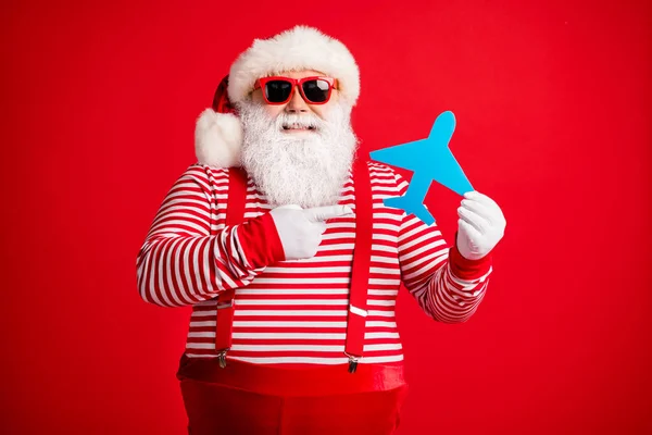 Foto do velho homem barba cinza segurar dedo direto papel plano sorriso desgaste santa claus x-mas fantasia suspensórios sol listrado camisa boné isolado cor vermelha fundo — Fotografia de Stock