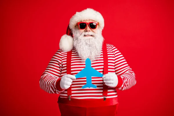 Foto do velho homem cinza barba segurar demonstrar mostrando azul papel avião engraçado desgaste santa claus x-mas fantasia suspensórios sol listrado camisa tampa isolado vermelho cor fundo — Fotografia de Stock