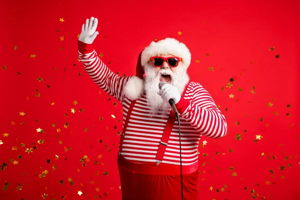 Фотографія дідуся сіра борода тримає мікро-відкритий рот підняти руку співати пісню подія носити Санта-Клауса підвіски для костюмів сонячної скляної смугастої сорочки ізольований червоний колір фону — стокове фото