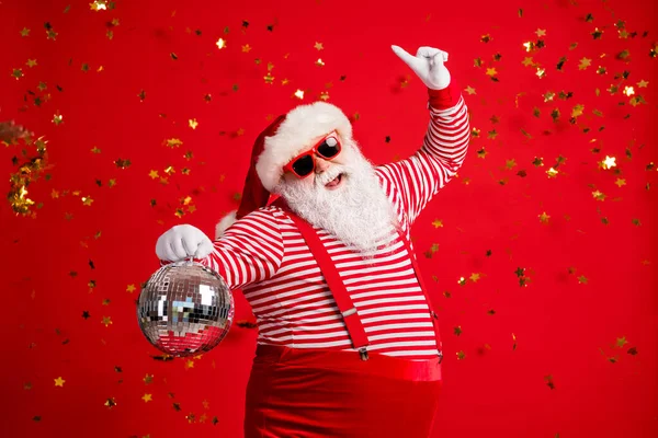 Фото пенсіонерки старий сірий борода тримає ретро диско м'яч танець підняти палець носити Санта х-рік костюм підвіски сонцезахисні окуляри рукавички смугаста сорочка шапка ізольований червоний колір фону — стокове фото