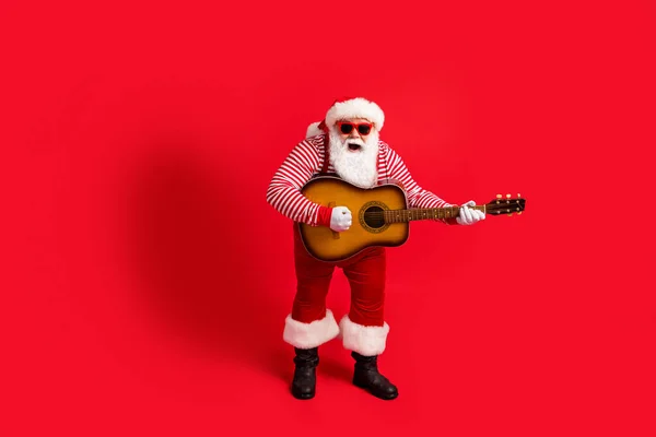 Full length foto di pensionato vecchio giocare chitarra bocca aperta cantare performance usura bretelle costume di Babbo Natale camicia a righe occhiali copricapo stivali isolato colore rosso sfondo — Foto Stock