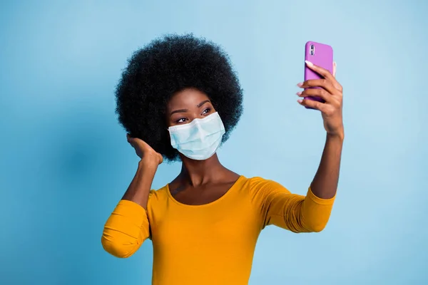 Foto-Porträt von ziemlich dunkelhäutigen Mädchen unter Selfie Touch Frisur tragen medizinische Maske isoliert blaue Farbe Hintergrund — Stockfoto