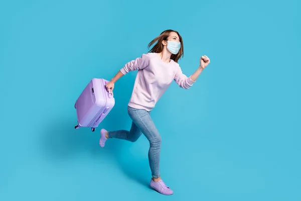 Foto lateral de perfil de longitud completa de una chica positiva corriendo sosteniendo una maleta púrpura con máscara facial azul aislada sobre fondo de color azul —  Fotos de Stock