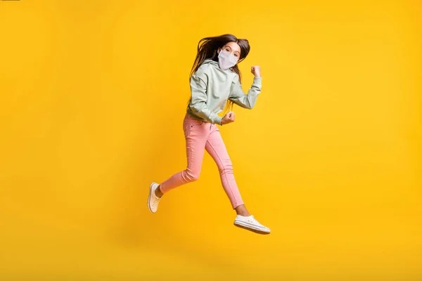 Teljes hosszúságú fotó a kislány ugrás kéz ököl fel divatos kapucnis viselni fehér arc maszk elszigetelt sárga színű háttér — Stock Fotó