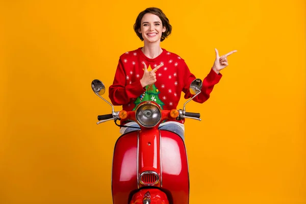 Foto van positief meisje in kerst boom decor trui trui rijden scooter punt twee vingers copyspace x-mas avond noel advertenties geïsoleerd over heldere glans kleur achtergrond — Stockfoto