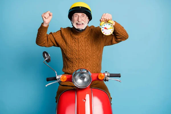 Portrait of his he nice attractive cheerful glad successful bearded grey-haired man courier riding moped holding in hand clock punctuality on-time delivery isolated over blue pastel color background