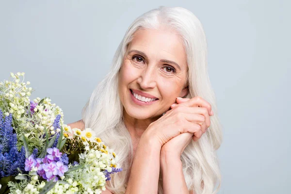 Güzel, çekici, emekli bir kadın koca bir demet yabani çiçeğin tadını çıkarıyor. Güzel, izole edilmiş gri bir arka plan. — Stok fotoğraf