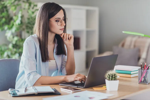 Foto di pensoso giovane signora sedersi desktop dito mento guardare computer portatile viso calmo indossare occhiali camicia in ufficio a casa all'interno — Foto Stock