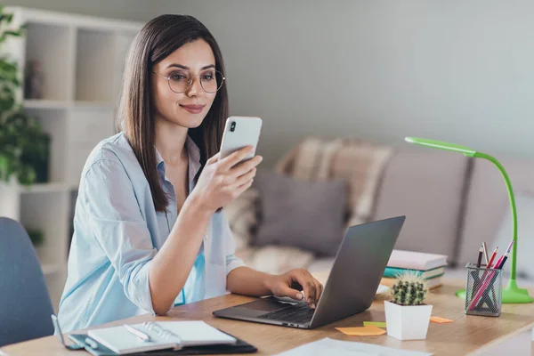 Foto de adorável jovem senhora segurar telefone olhar tela palma teclado usar óculos camisa em casa escritório dentro de casa — Fotografia de Stock
