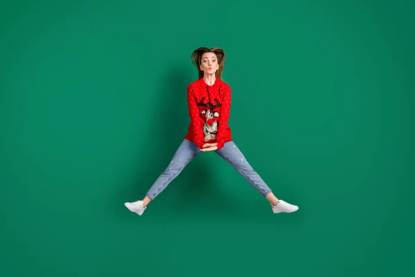 Фотографія повного тіла досить фанк-гарненька леді стрибає високо поширені ноги x-mas вечірка посилає повітряні поцілунки кокетливий настрій носіння оленя червоний потворний орнамент светр джинси ізольовані зелений колір фону — стокове фото