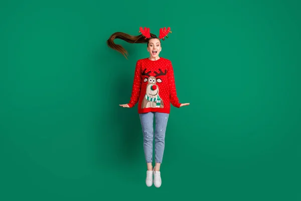 Фотографія повного розміру приваблива смішна мила леді стрибає високі Різдвяні вечірки гарний настрій одяг для оленів головні убори роги червоний потворний орнамент светр джинси взуття ізольовані зелений колір фону — стокове фото