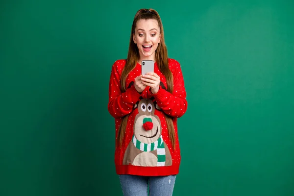 Photo of attractive shocked excited lady hold telephone open mouth read post comments new followers wear red ugly ornament deer decor pullover jeans isolated green color background — Stock Photo, Image