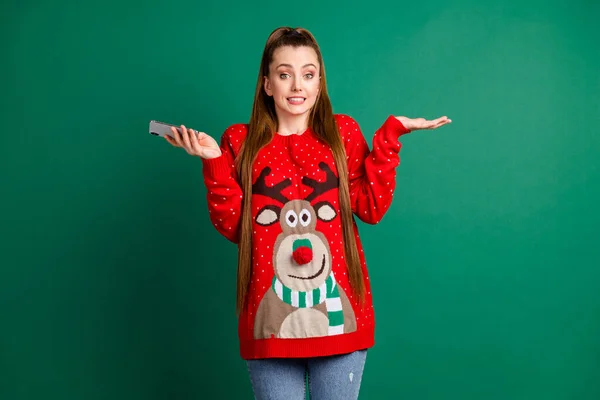 Sorry guys. Photo of attractive lady hold telephone chatting friends newyear party cancelled shrug shoulders wear red ugly ornament deer decor pullover jeans isolated green color background — Stock Photo, Image